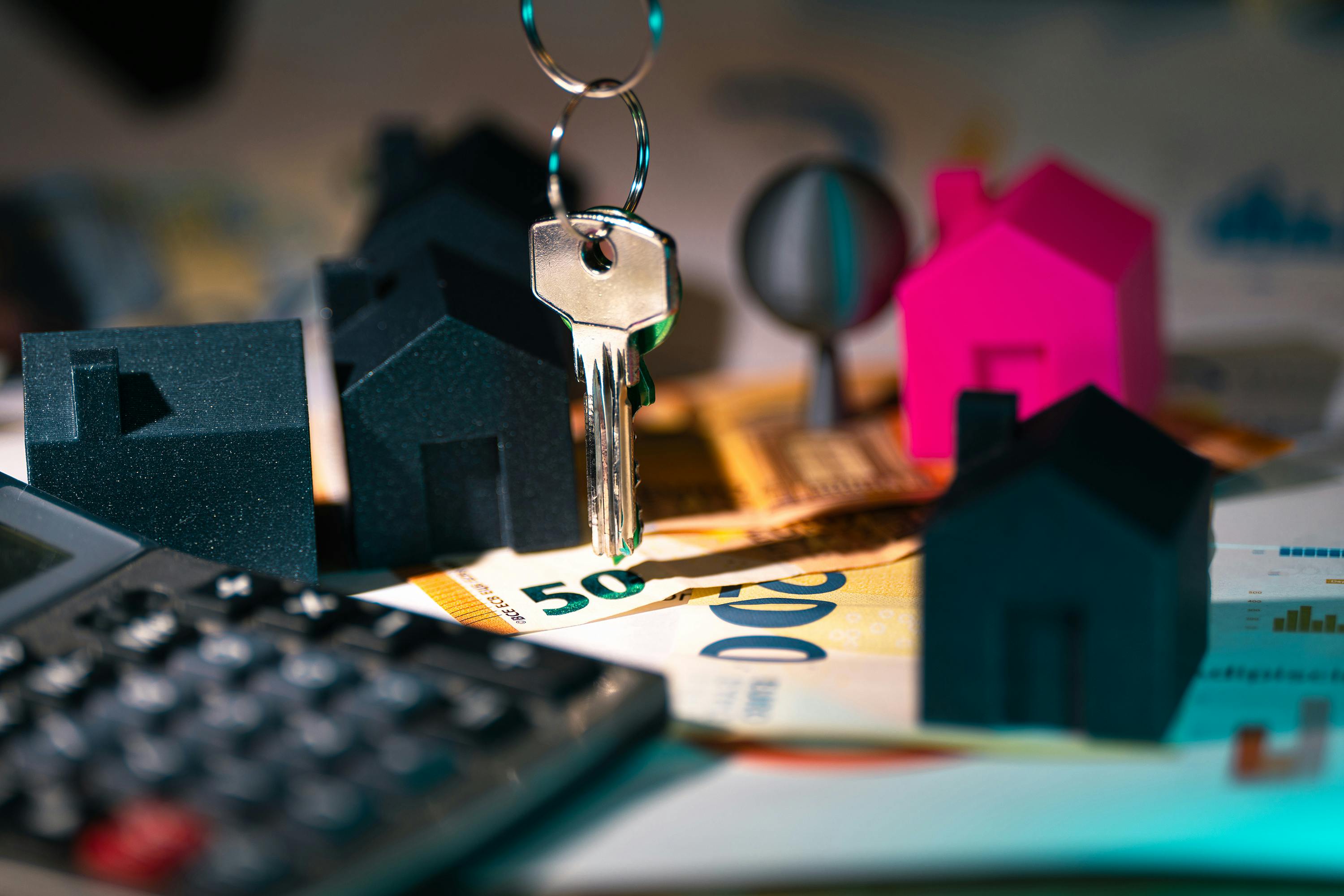 A hand holding a house key beside a model home, illustrating how a higher income still has to face the full housing cost stack.