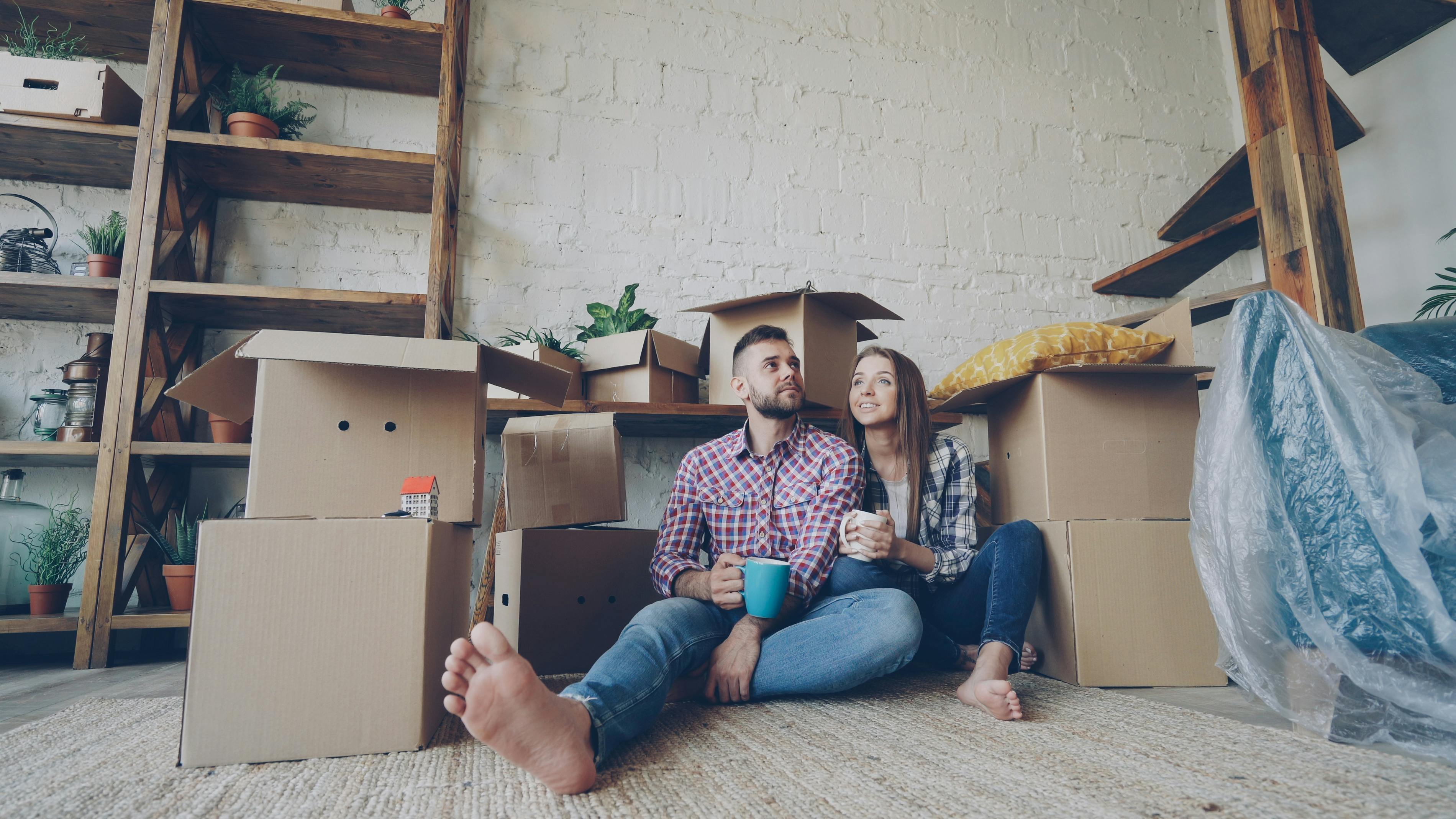 A young couple sitting among moving boxes in a new home, representing the move-in costs and transition period after closing.