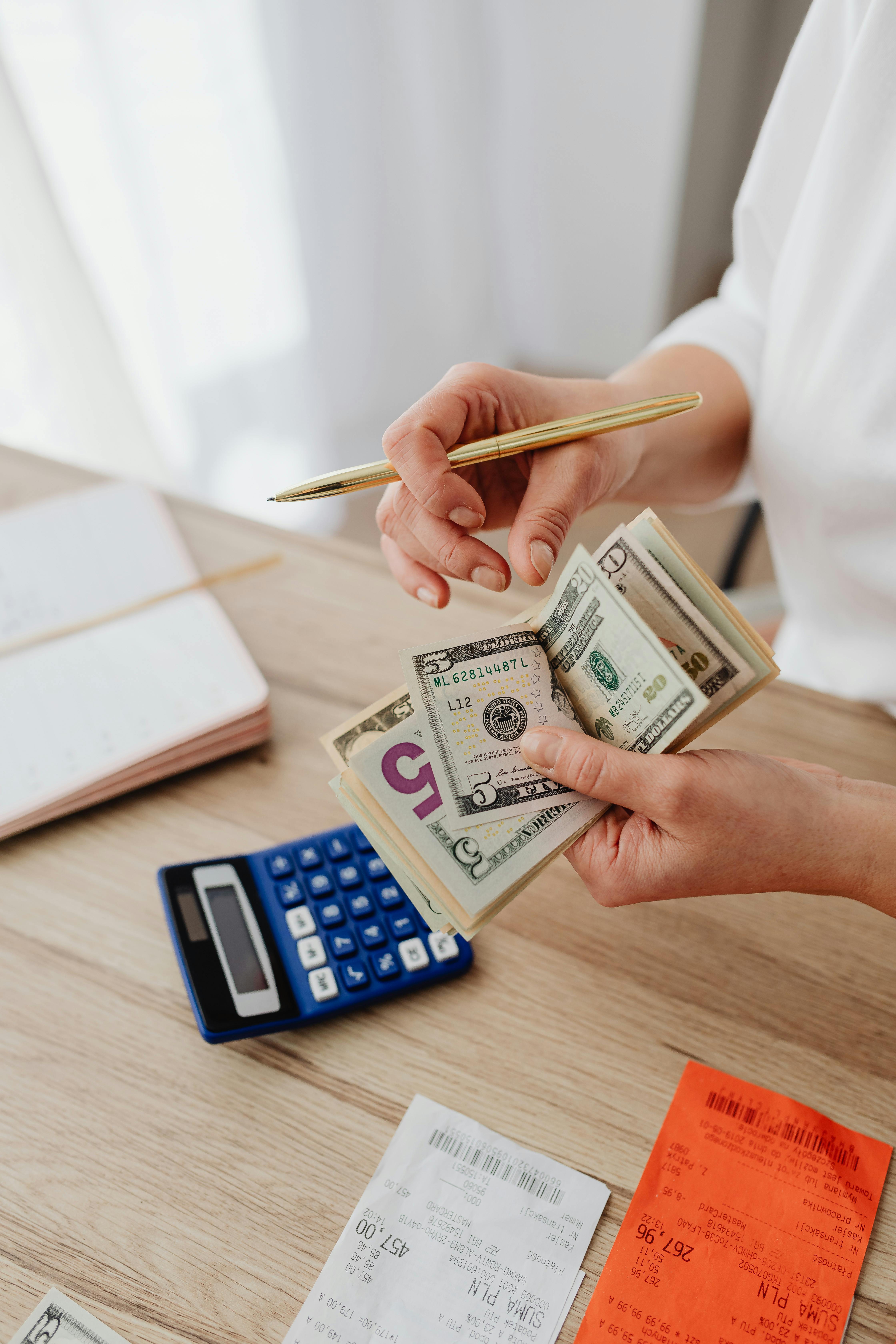A woman counting cash beside a calculator and receipts while reviewing a household budget.